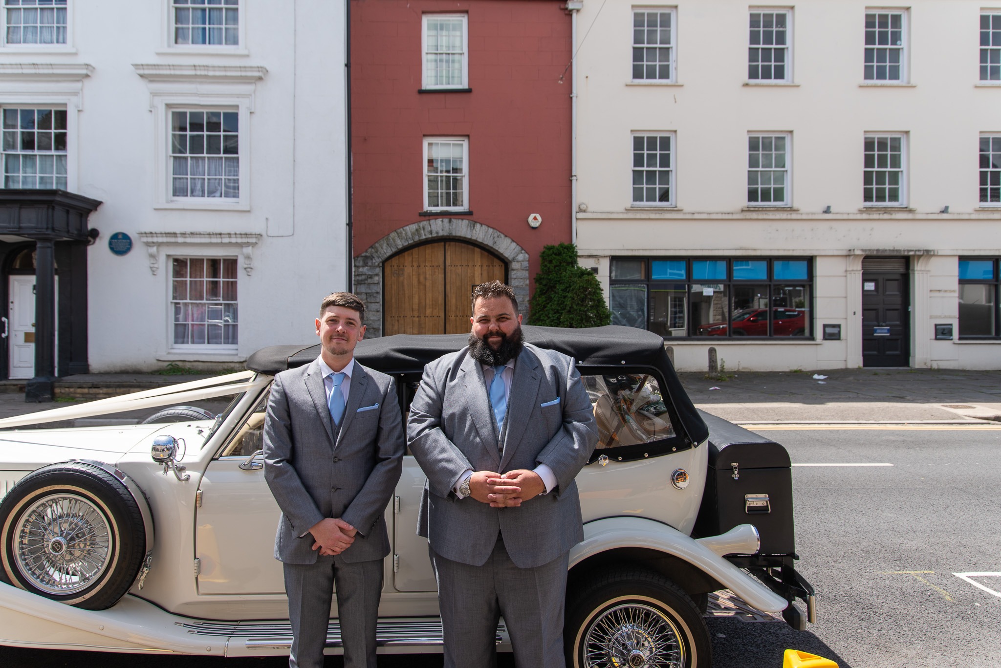 The groom and best man in matching grey suits standing by a vintage wedding car outside the Bear Hotel in Cowbridge, photographed by South Wales wedding photographer Charlie Hannah
