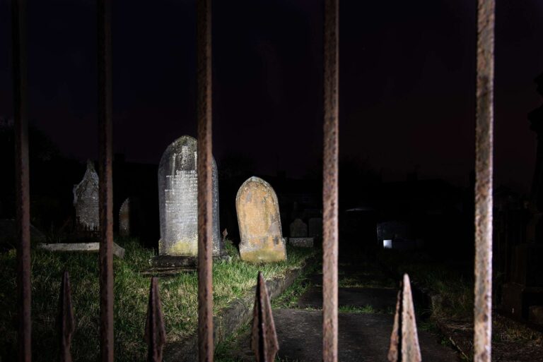 Fine art night photography of historic headstones through iron gates, from Charlie Hannah's Alone in My Head project.
