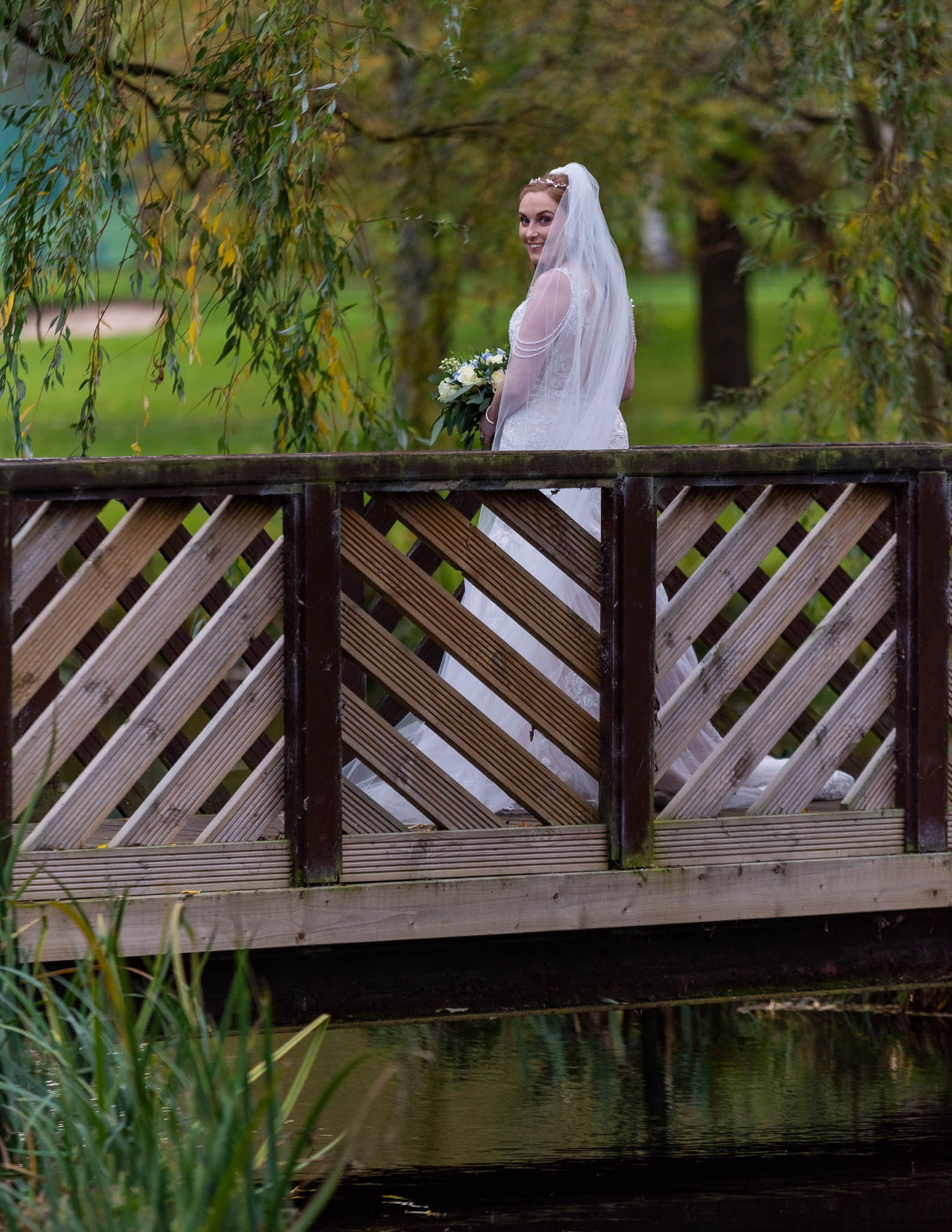 Bride Amy standing on a wooden bridge in Sutton Coldfield, captured in a relaxed, natural documentary style.