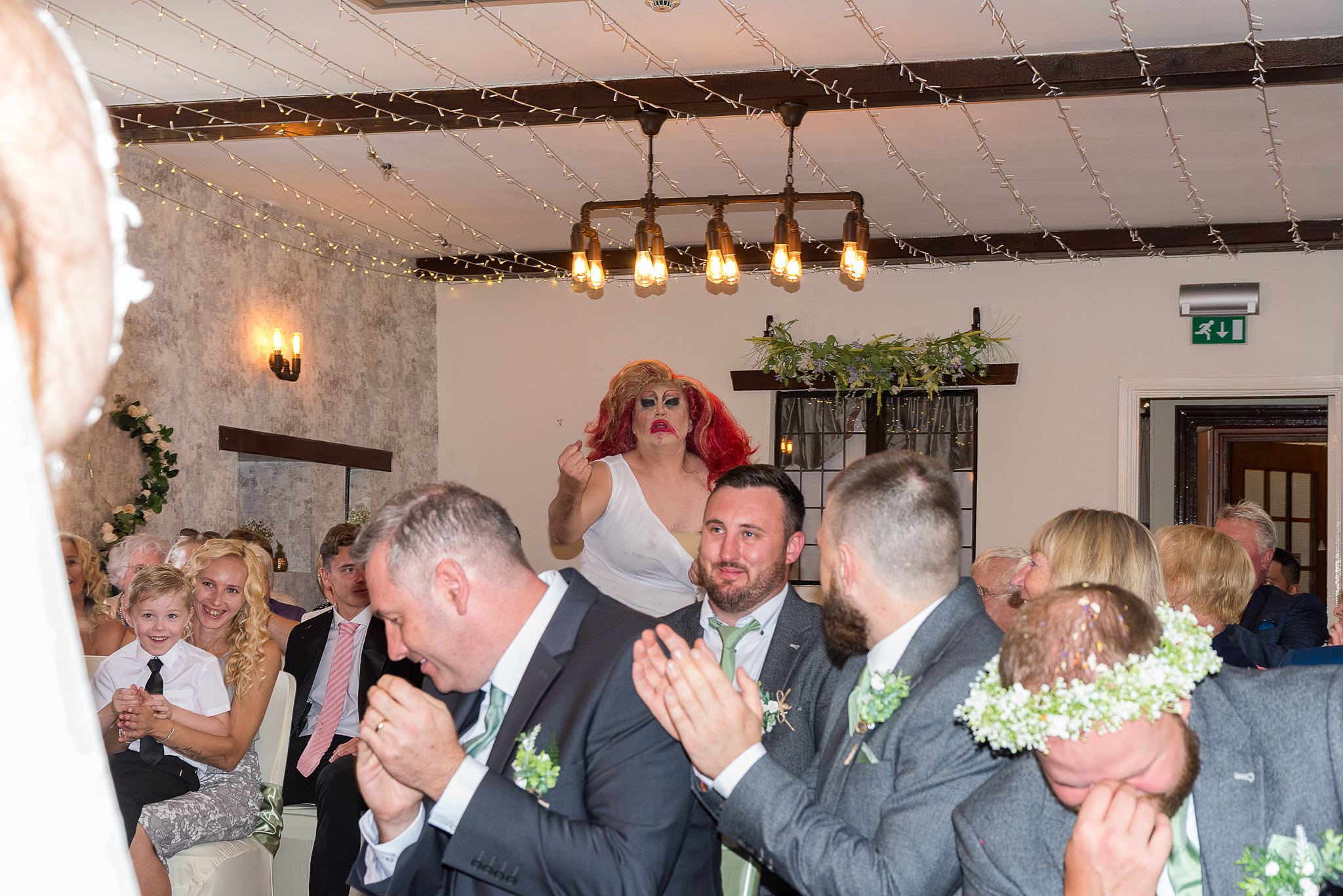 Documentary wedding photography capturing the joyful reaction of guests to a surprise drag queen's entrance just after the imperial march during a wedding ceremony in South Wales.
