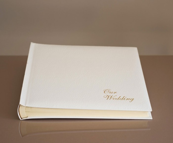 St James Classic white leather wedding album with gold foil lettering resting on a surface, offered by South Wales wedding photographer Charlie Hannah