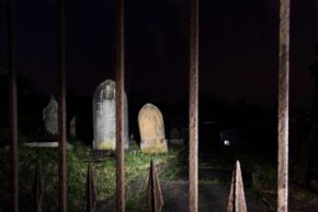 Fine art night photography of historic headstones through iron gates, from Charlie Hannah's Alone in My Head project.