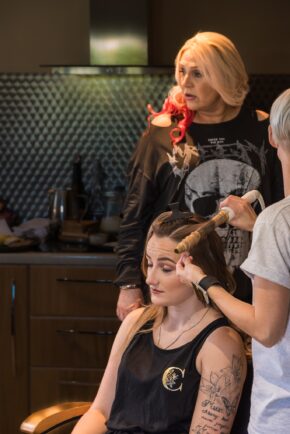 A candid documentary photo capturing a concerned or amused expression in the background while hair is being curled during wedding morning prep.