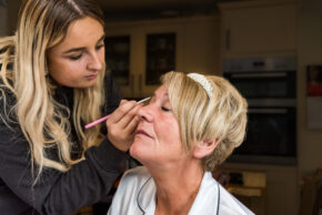 A candid documentary photo of professional makeup artist Jaz applying makeup to a bridal party member during wedding morning prep.