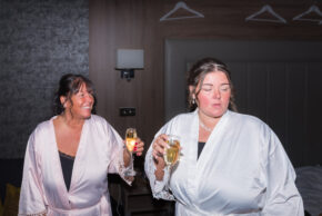 A candid, documentary-style photograph of a bride sharing a relaxed morning toast with her mum during bridal preparations, captured by Charlie Hannah.