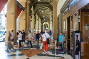 A long exposure street photograph showing the motion blur of people walking under historic arched columns in Florence, Italy.