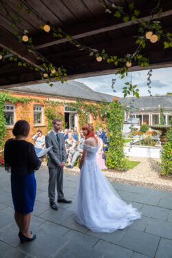 Authentic, documentary-style photography, capturing your promises in the beautiful landscapes of Norfolk The Vow – A bride and groom sharing intimate wedding vows during an outdoor ceremony in a beautiful Norfolk garden setting.