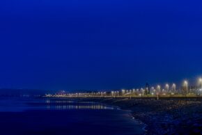 A long-exposure nightscape of Aberavon Beach showing an illuminated coastal promenade casting starburst reflections on the wet sand under a deep blue twilight sky.