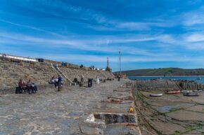 People relaxing on the stone harbour wall at Cei Newydd (New Quay) under a blue sky in Ceredigion, Wales