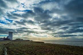 A white lighthouse standing on a coastal cliff under a dramatic, cloudy sky overlooking the sea.