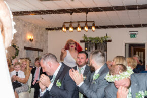 Documentary wedding photography capturing the joyful reaction of guests to a surprise drag queen's entrance just after the imperial march during a wedding ceremony in South Wales.