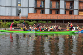 Action sports and community event photography capturing a synchronised dragon boat team competing on the water. A team of paddlers racing in a vibrant green dragon boat on the River Avon in Stratford-upon-Avon.
