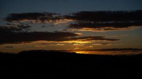 Llantrisant Vibrant sunset or sunrise breaking through dramatic layers of dark clouds over a silhouetted landscape horizon.