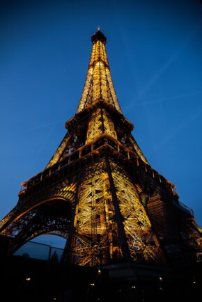 View striking night photography of the Eiffel Tower brilliantly illuminated in gold against a deep twilight blue sky in Paris, captured in February 2020 by Charlie Hannah. Low-angle view of the golden-illuminated Eiffel Tower against a deep blue twilight sky in Paris, February 2020.