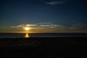 Capturing the golden glow of a coastal sunset on Jersey with a silhouette on the cliffs viewed from Grosnez Castle, A lone figure silhouetted on a cliff edge overlooking the sea during a dramatic sunset on the island of Jersey