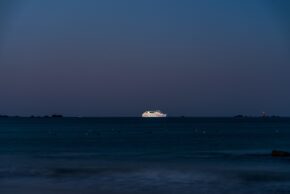 Jersey - August 2022 A brightly lit ship glowing on the dark sea during early morning twilight off the coast of Jersey
