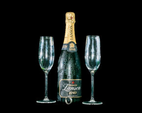 Explore elegant commercial and still life photography by Charlie Hannah, featuring a chilled bottle of Lanson champagne and crystal flutes styled for a special celebration. Still life photography of a chilled bottle of Lanson champagne covered in condensation, flanked by two empty champagne flutes and a ring at the base, isolated against a black background.