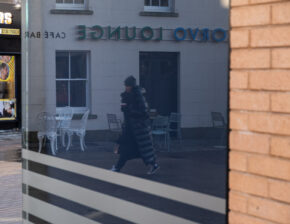 Conceptual street photography from a reflections project, showing a pedestrian captured as a reflection in a glass shop window in the city.