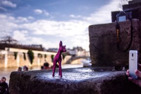 Paris - February 2020 A tiny glittery pink toy deer figurine is set on a stone wall by a river in Paris while someone photographs it with a smartphone, street photography.