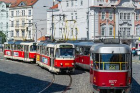 Urban street photography capturing classic red-and-cream trams on a cobblestone square in Prague surrounded by historic European buildings.