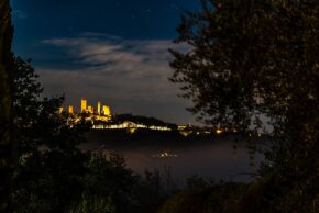 San Gimignano, Tuscany, Sept 2023 The illuminated medieval towers of San Gimignano perched on a hill under a starry night sky, framed by dark trees