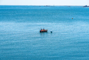 A small fishing boat with people on board floating on a vast blue sea under a clear sky