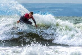 Llantwit Major A surfer wearing a wetsuit carving through a crashing ocean wave with vibrant white sea spray.