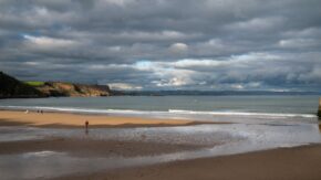 People walking dogs along the wide sandy expanse of Tenby beach under a dramatic cloudscape in Pembrokeshire