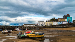 Fishing boats and a yellow catamaran resting on the harbor sand in Tenby at low tide beneath a dramatic cloudy sky