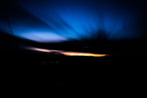 Beddau - Febrary 2020 Night landscape photography capturing a deep blue sky with radiating cloud streaks above a dark hill silhouette lined with distant wind turbines.