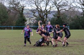 llantwit Fardre Action sports photography of a determined women's rugby player making a low tackle on an opponent during a match on a muddy pitch.