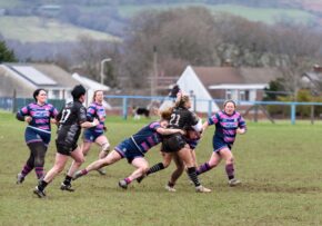 Llantwit Fardre Action sports photography of a women's rugby player carrying the ball and breaking through a tackle during a match on a muddy field.