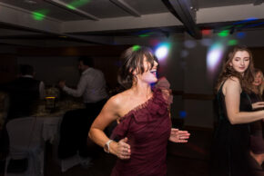 A candid, high-energy photograph of a guest laughing and dancing under colorful disco lights during an evening wedding reception, captured by Charlie Hannah.