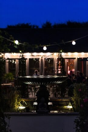 An illuminated stone garden fountain at night with string lights glowing in the background during an evening wedding reception