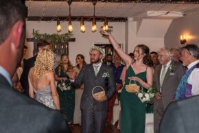 Guests throwing confetti indoors as a bride makes an entrance and wedding party members smile and hold small baskets during a wedding reception