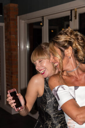 Mother and daughter laughing and dancing together during a joyful wedding evening reception.