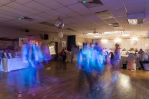 Blurred motion of wedding guests dancing on a wooden dance floor under a disco ball during an evening wedding reception party.