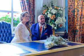 Bride and groom sitting side-by-side at a desk during their wedding ceremony register signing.