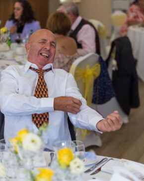 Candid wedding reception photo of a guest laughing and rolling up his sleeves during the celebrations, captured by South Wales photographer Charlie Hannah.