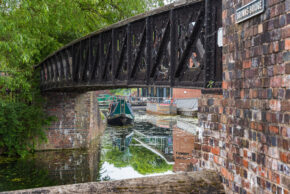Fine art canal photography by Charlie Hannah ARPS, featuring the dark iron lattice framework of Browns Bridge crossing over a reflective British canal.