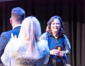 An award winner smiling and holding a trophy on stage during a ceremony in Cardiff, photographed by South Wales event photographer Charlie Hannah