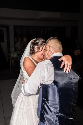 Bride and groom sharing an intimate embrace and laughing together during their first dance at the evening wedding reception.