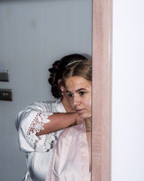 Bridesmaid wearing a pink satin robe having her hair and dress styled on the wedding morning.
