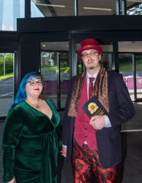 Two guests posing with an award, featuring a gentleman in a top hat and patterned trousers and a woman in a green dress, photographed by South Wales event photographer Charlie Hannah