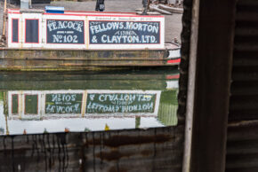 Fine art canal photography by Charlie Hannah ARPS, capturing the detailed historic signage of a Fellows, Morton & Clayton Ltd narrowboat reflected in the calm canal water.