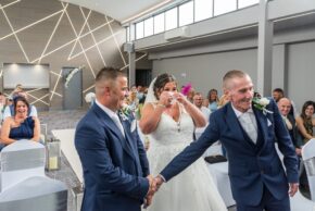 Emotional bride wiping away tears while the groom shakes hands with the father of the bride at the wedding ceremony.