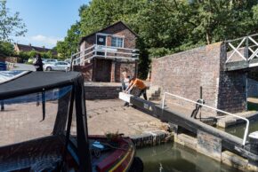 Fine art canal photography by Charlie Hannah ARPS, showing boaters working together to operate a heavy wooden lock gate next to a traditional red brick lock house.