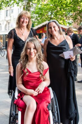 Three attendees posing outside St David's Hall in Cardiff during an event, with one seated in a wheelchair in a red dress, photographed by South Wales event photographer Charlie Hannah