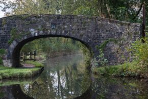 Fine art canal photography by Charlie Hannah ARPS, featuring an old stone bridge arch numbered 75 with a symmetrical reflection cast across the smooth canal surface.