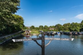 Fine art canal photography by Charlie Hannah ARPS, featuring a classic black and white wooden fingerpost pointing toward the Stratford and Grand Union canals under a bright blue sky.